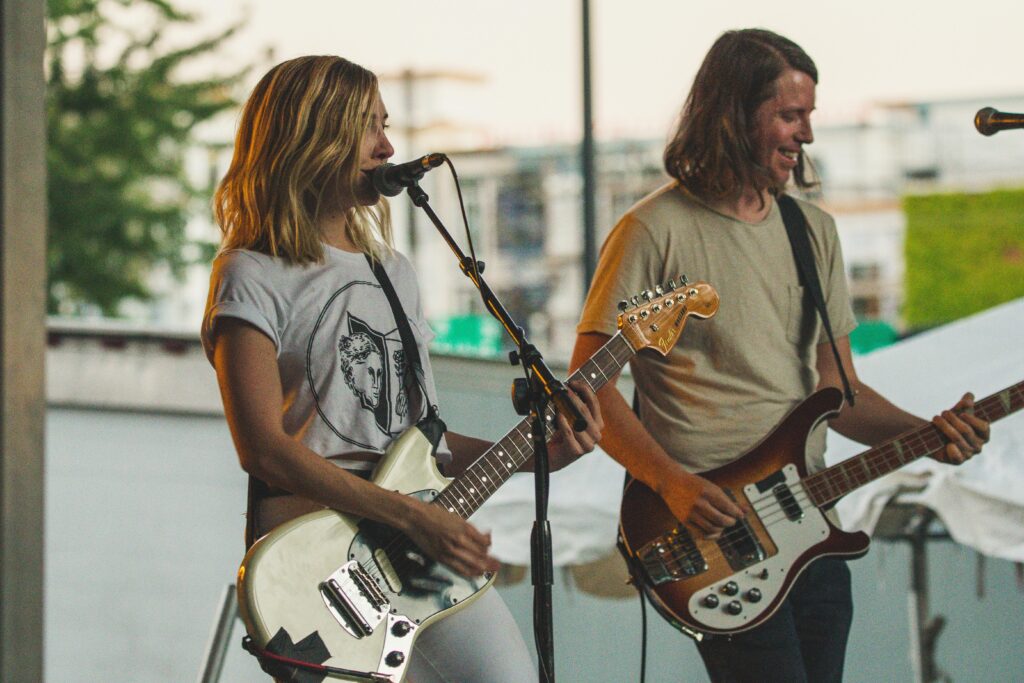 Live outdoor performance featuring male and female guitarists on stage playing music.