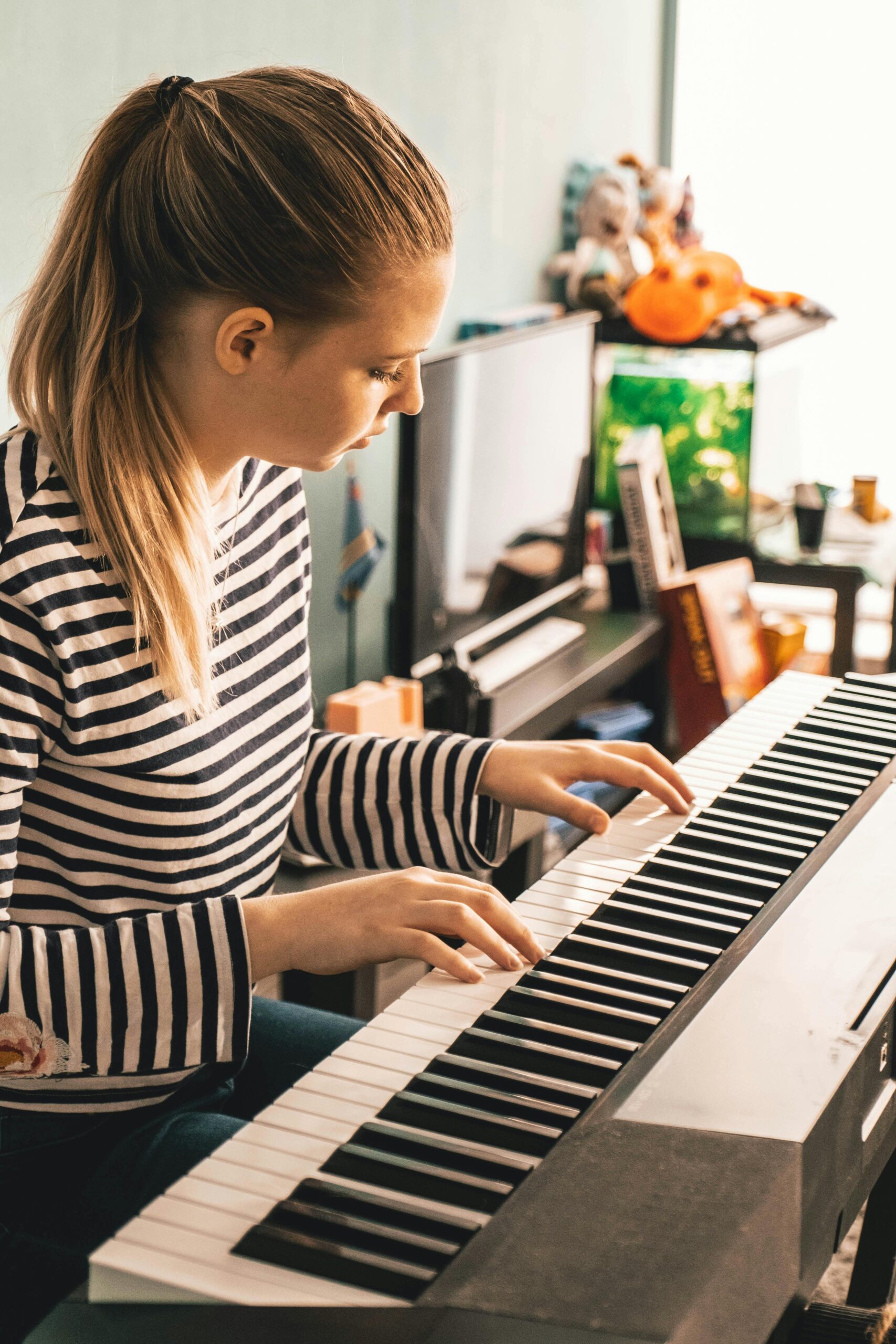 A woman in a striped shirt playing a piano in a cozy indoor setting.