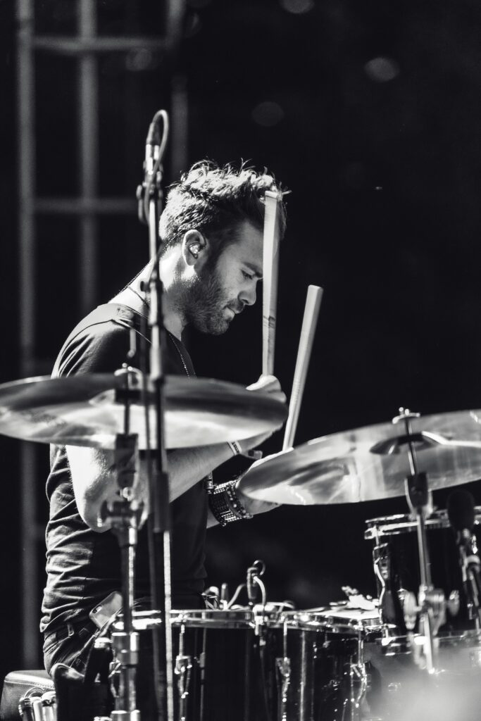 Black and white photo of a drummer performing passionately during a live music concert.