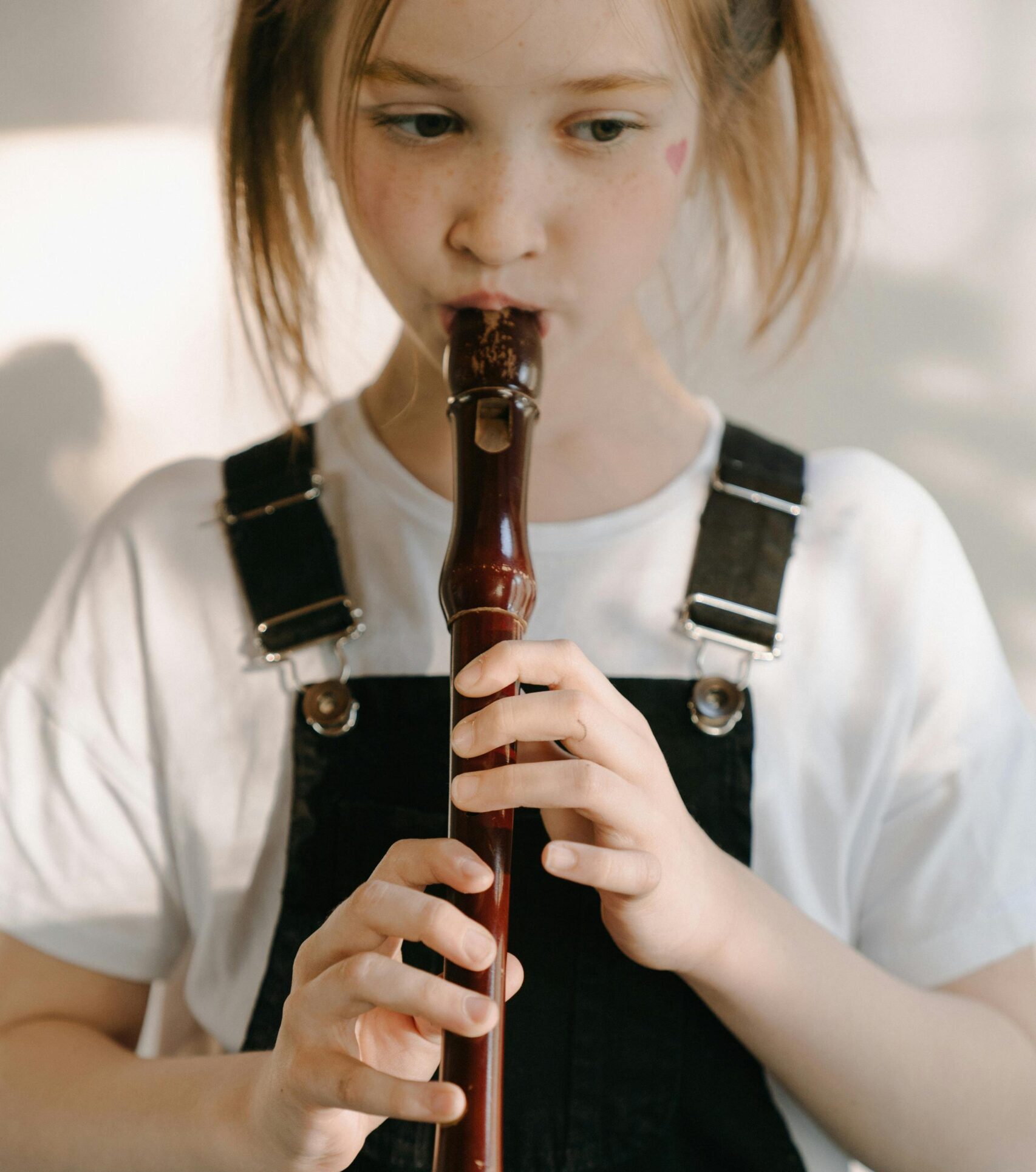 A young girl practicing the recorder, focusing on her music indoors with natural light.